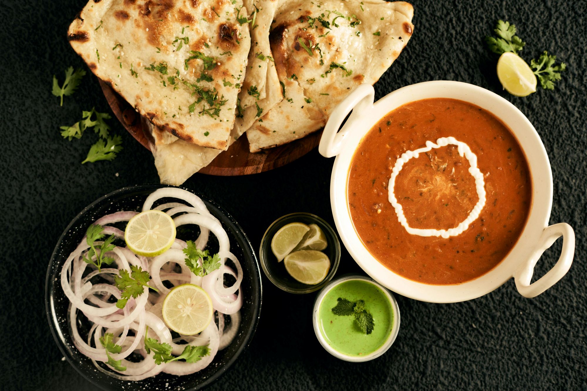 An appetizing Indian meal featuring naan, creamy curry, and fresh condiments
